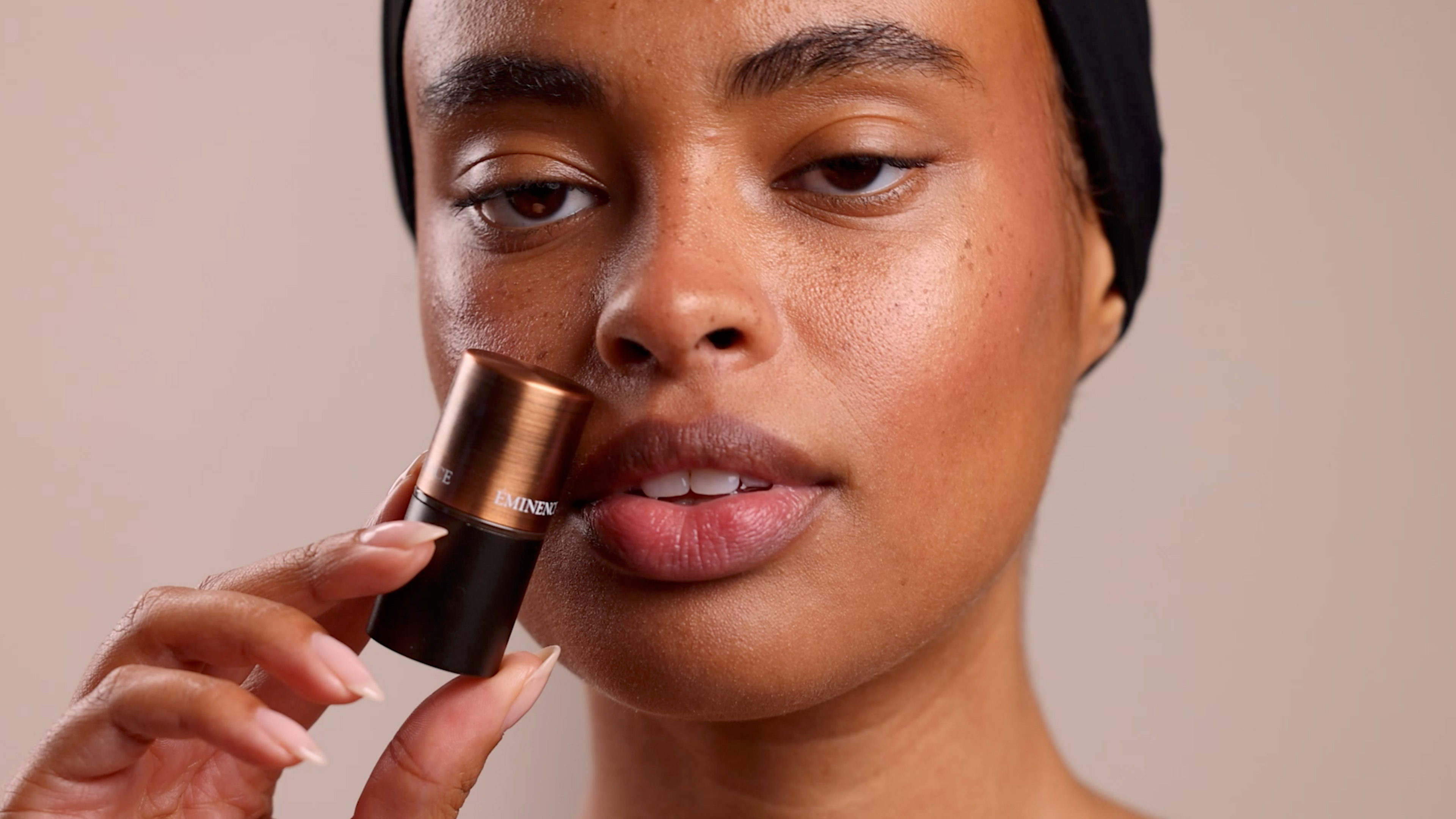 A woman holding the Eminence Organics Rosehip & Lemongrass Lip Balm SPF 15 close to her face