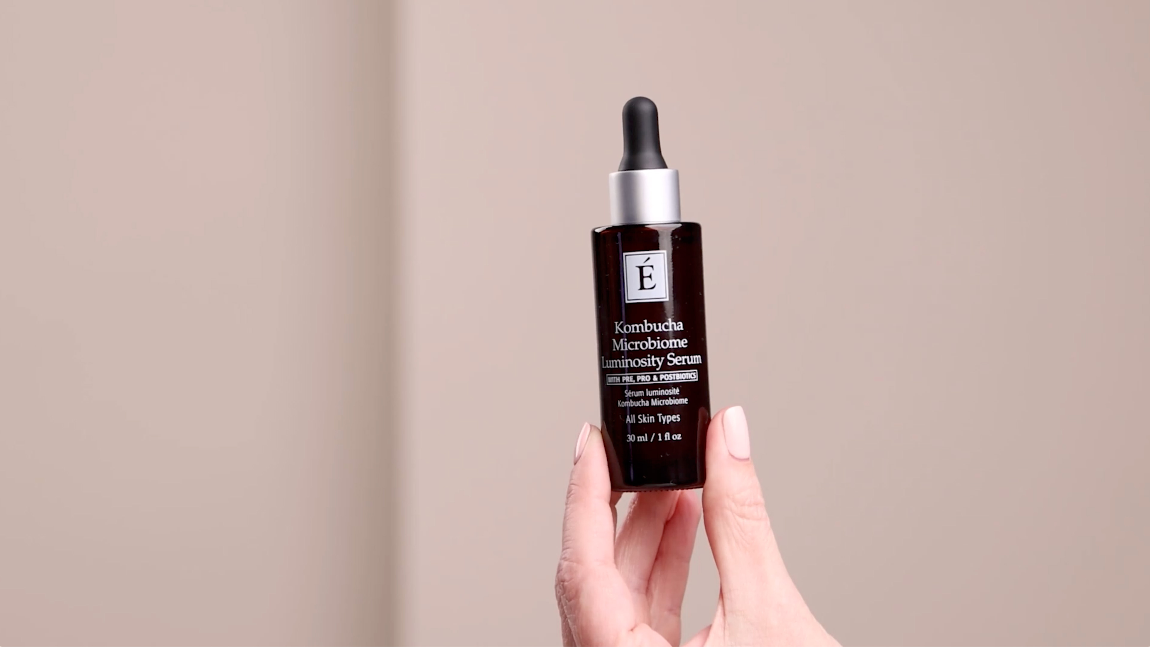 A hand holding the Eminence Organics Kombucha Microbiome Luminosity Serum bottle