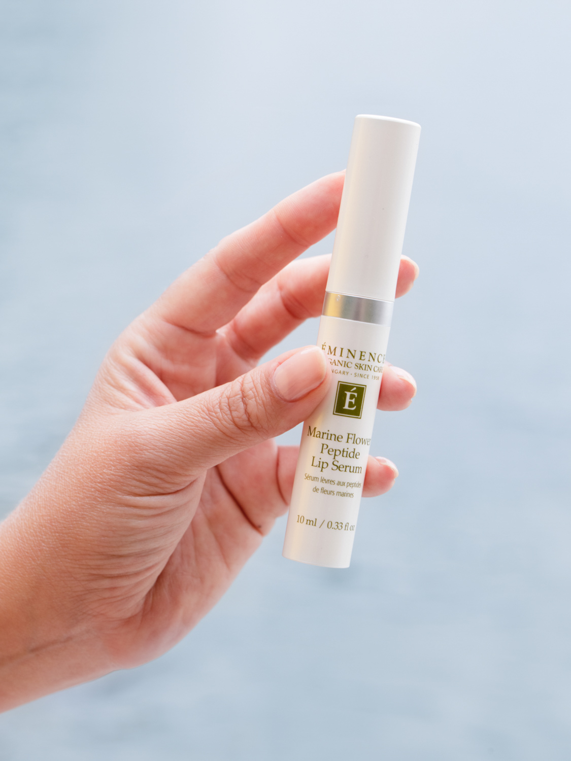A hand holding the Eminence Organics Marine Flower Peptide Lip Serum tube