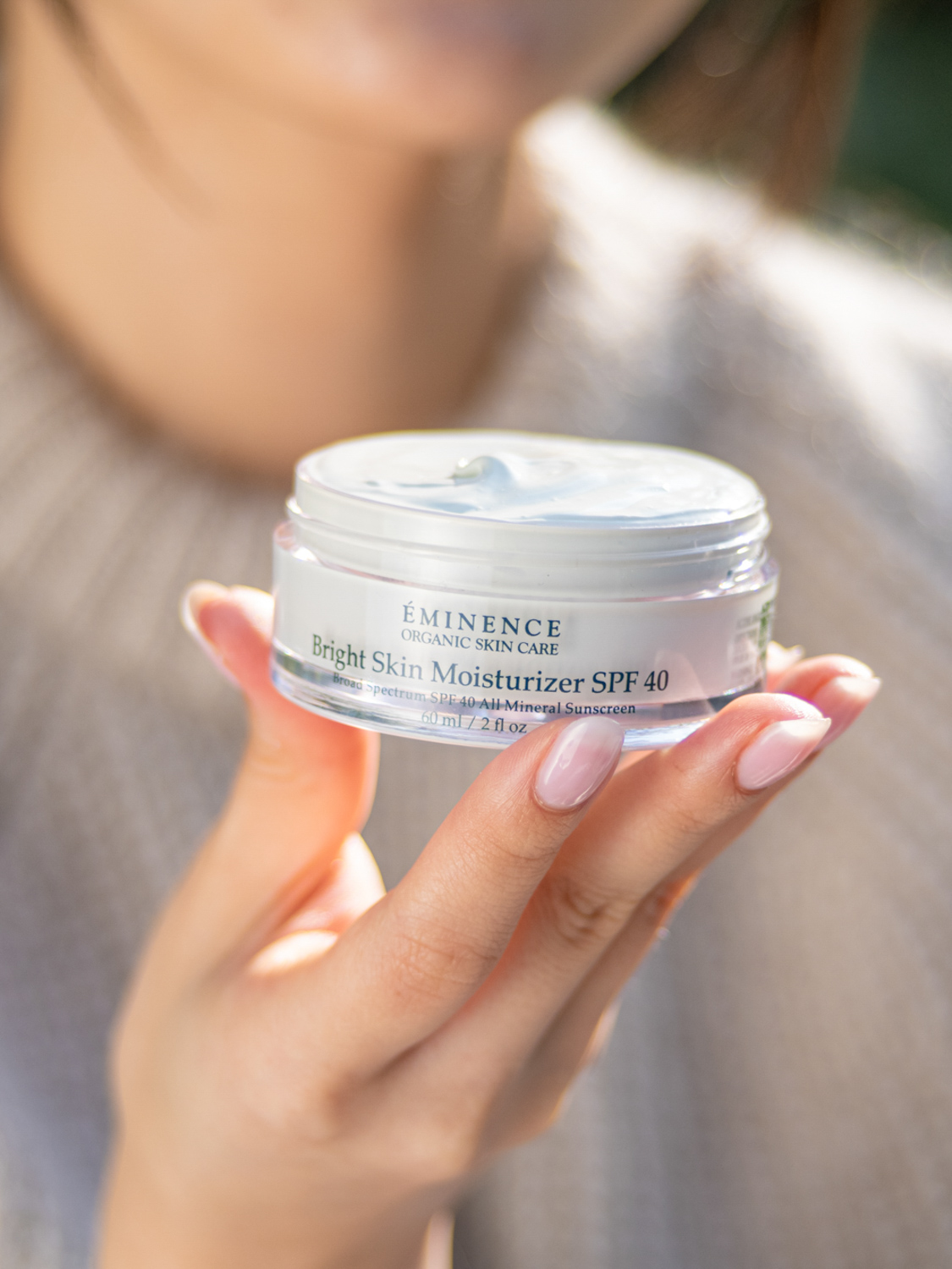 A woman holding Eminence Organics Bright Skin Moisturizer SPF 40