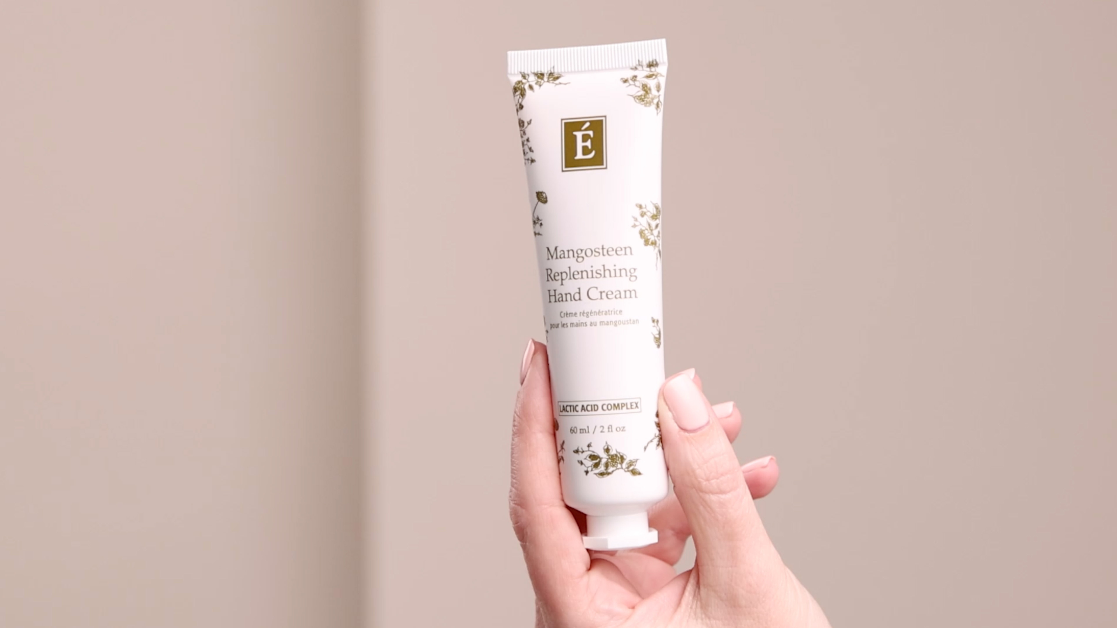 A hand holding the Eminence Organics Mangosteen Replenishing Hand Cream tube