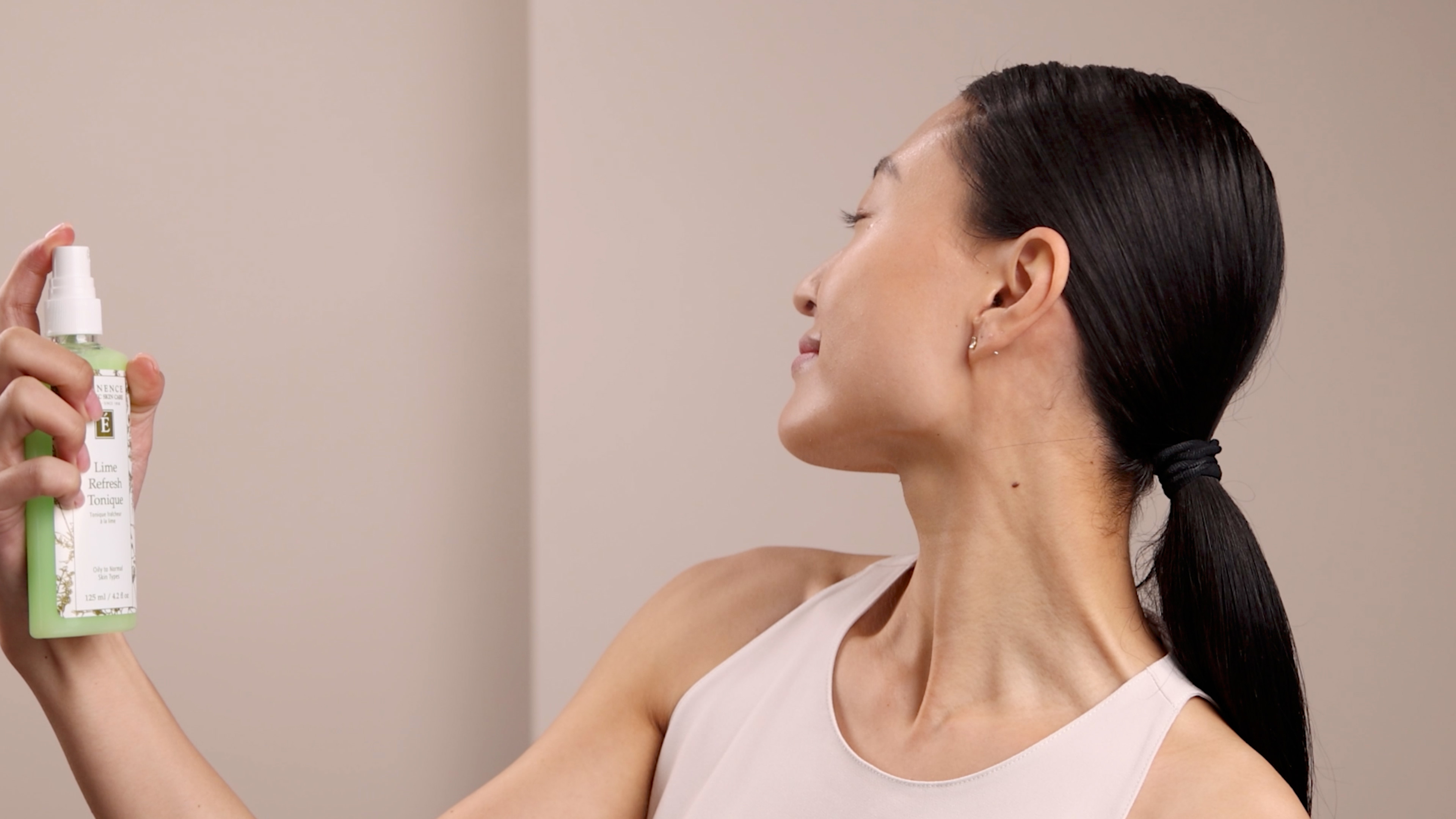 A woman spraying the Eminence Organics Lime Refresh Tonique onto her face