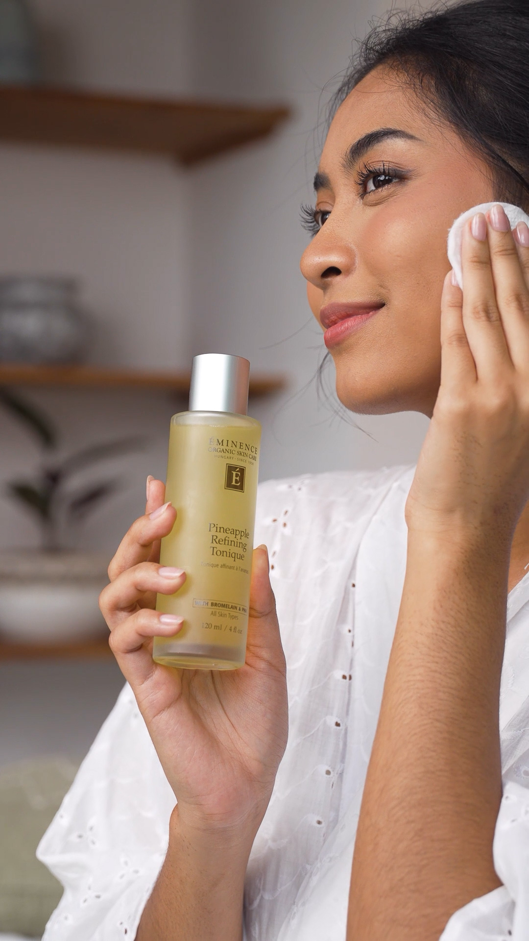 A woman holding the Eminence Organics Eminence Organics Pineapple Refining Tonique and applying the tonique on her face
