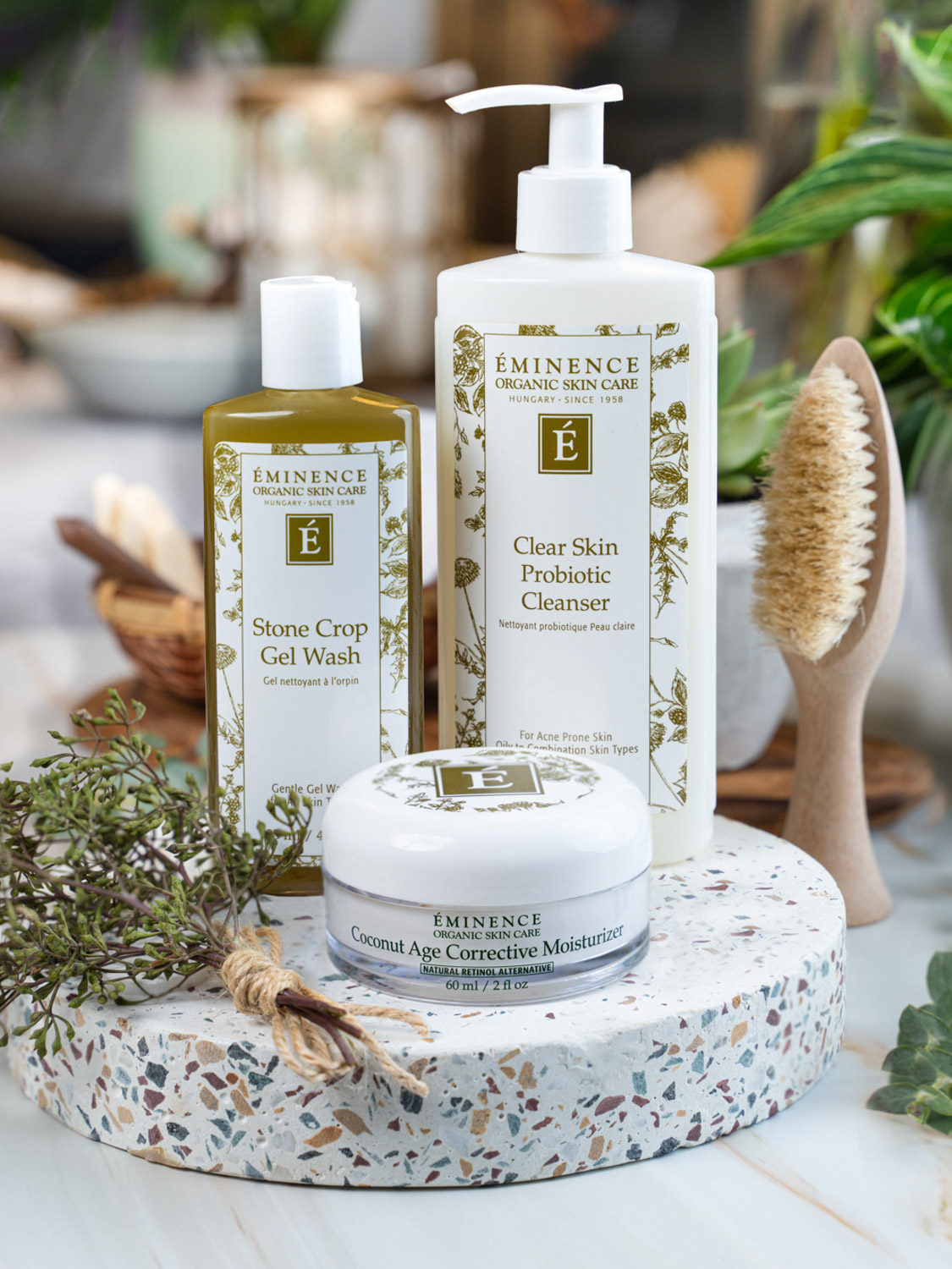 3 Eminence Organics products displayed with a brush and plants