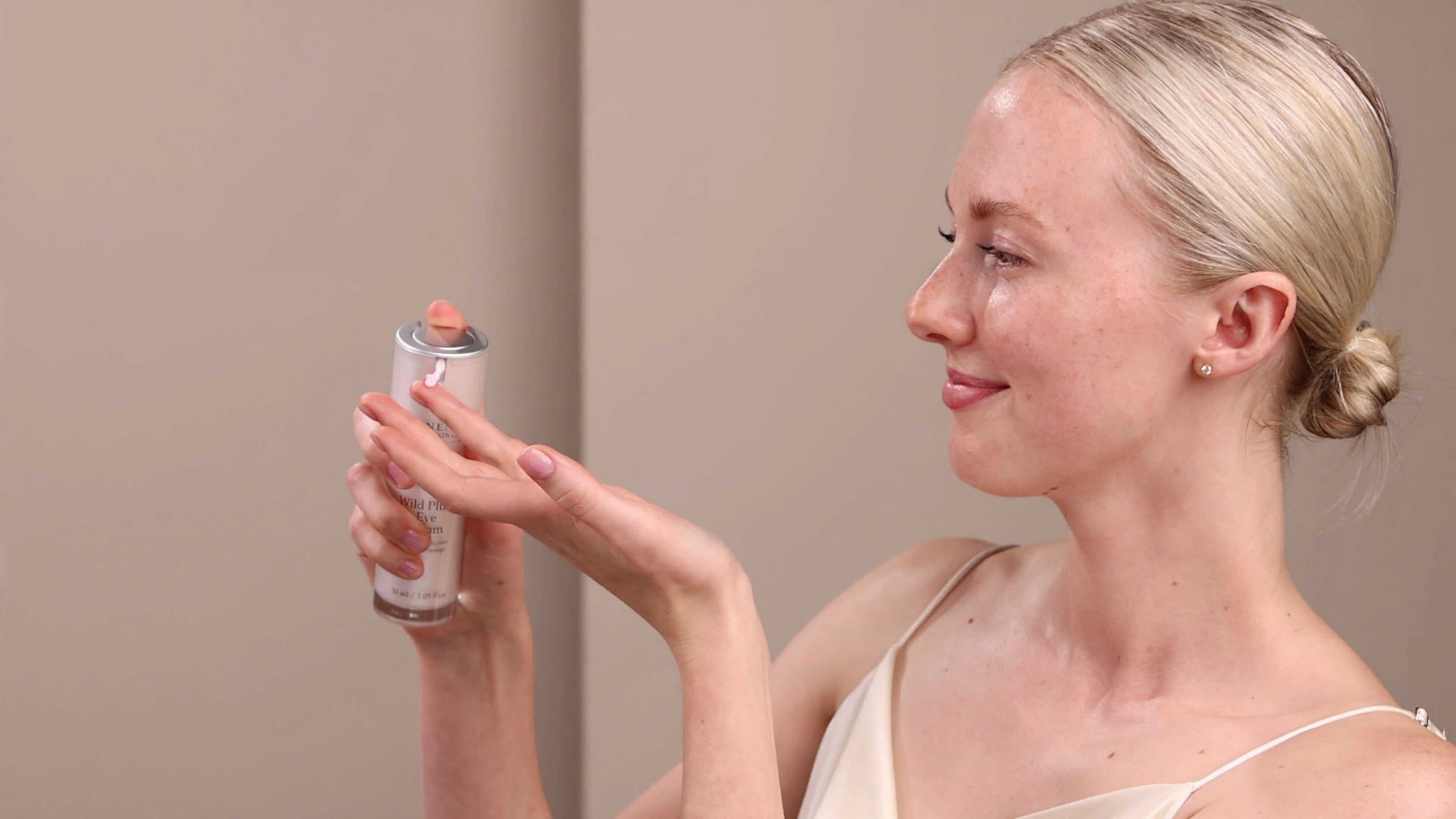 A woman dispensing a small amount of the Eminence Organics Wild Plum Eye Cream onto her hand from a pump component