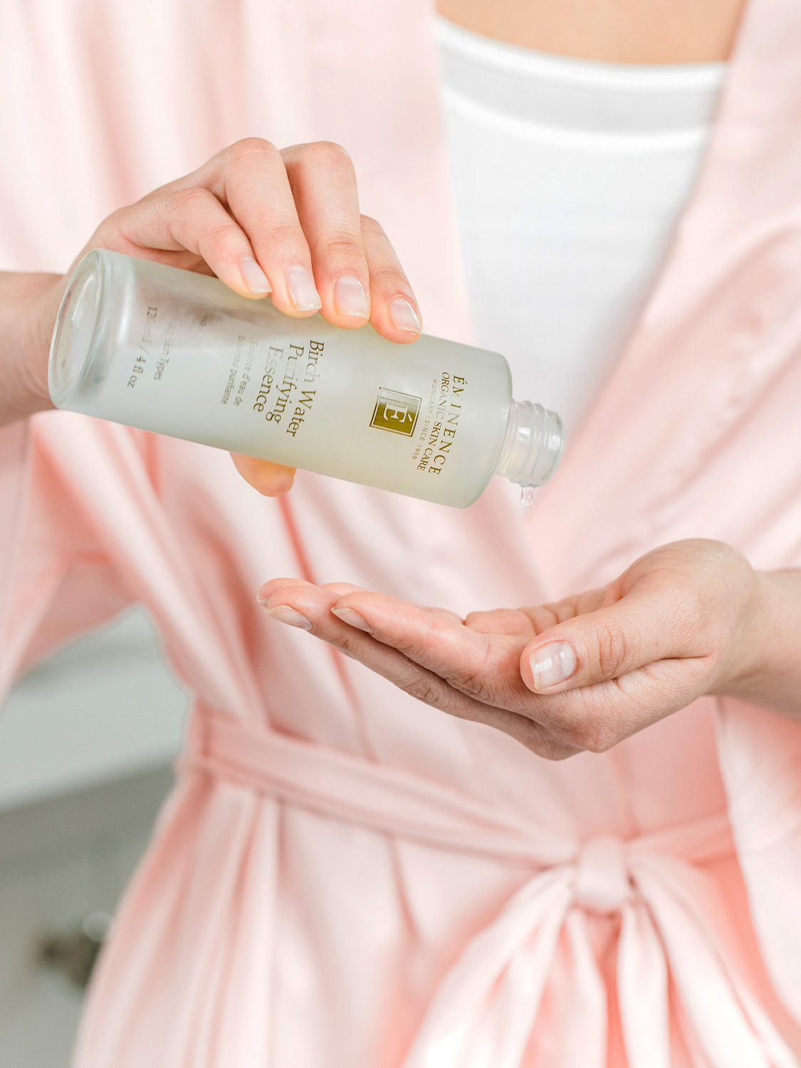 A woman pouring Eminence Organics Birch Water Purifying Essence into hand