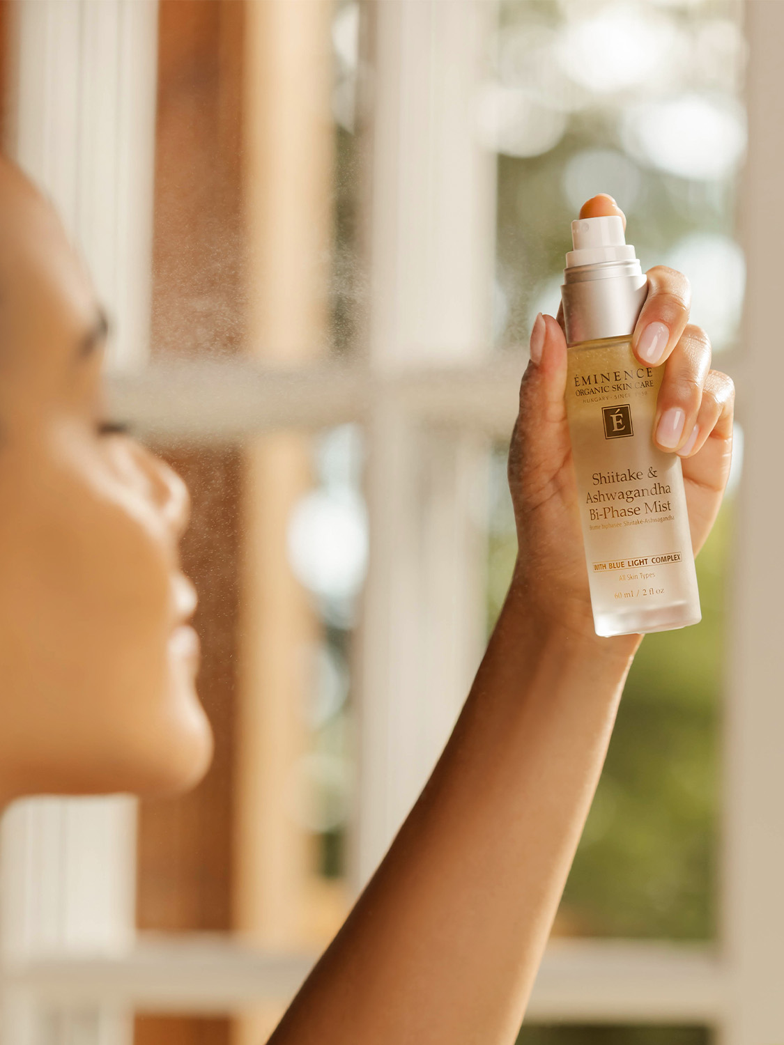 A woman holding Eminence Organics Shiitake & Ashwagandha Bi-Phase Mist 