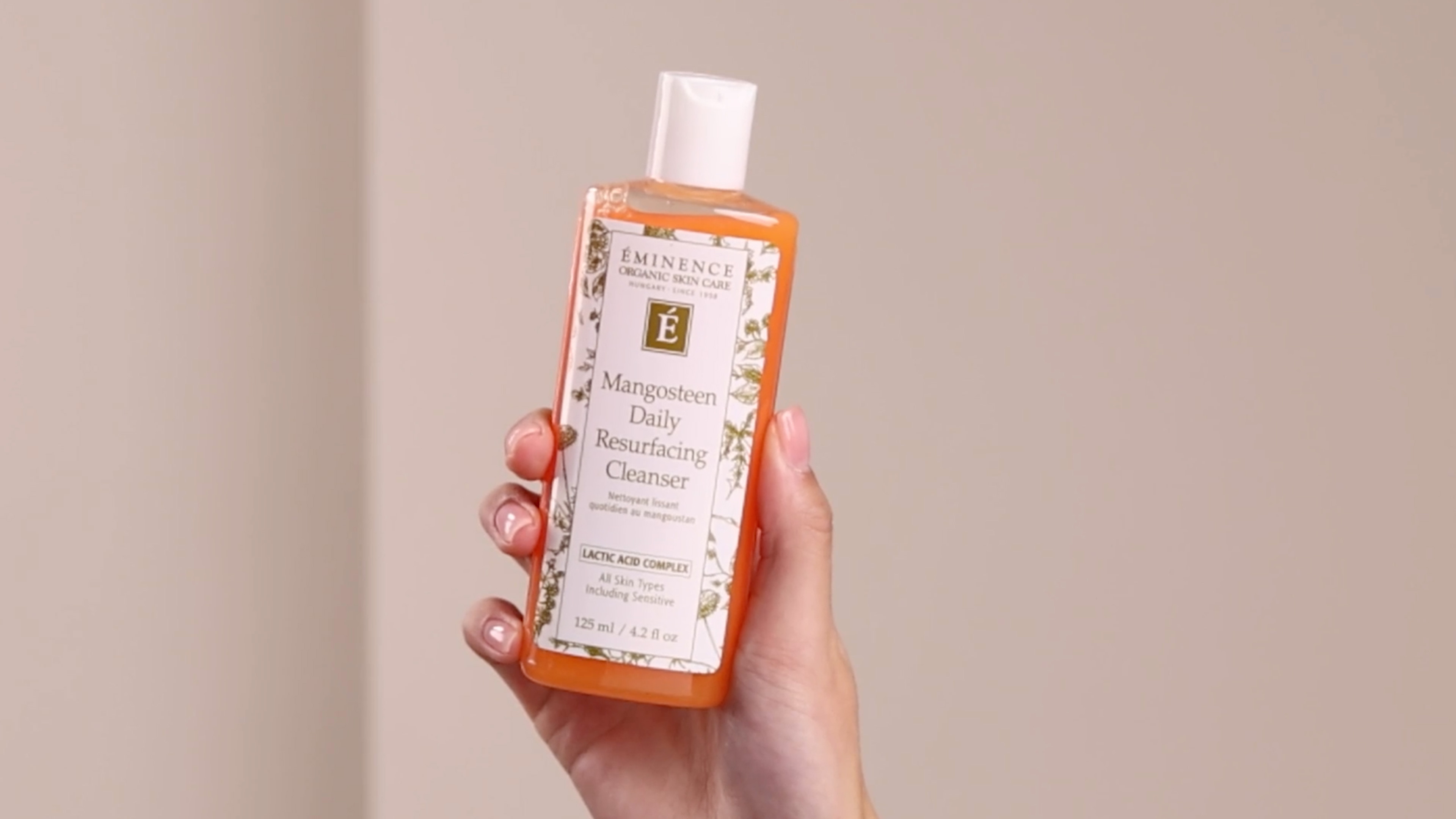 A hand holding the Eminence Organics Mangosteen Daily Resurfacing Cleanser bottle