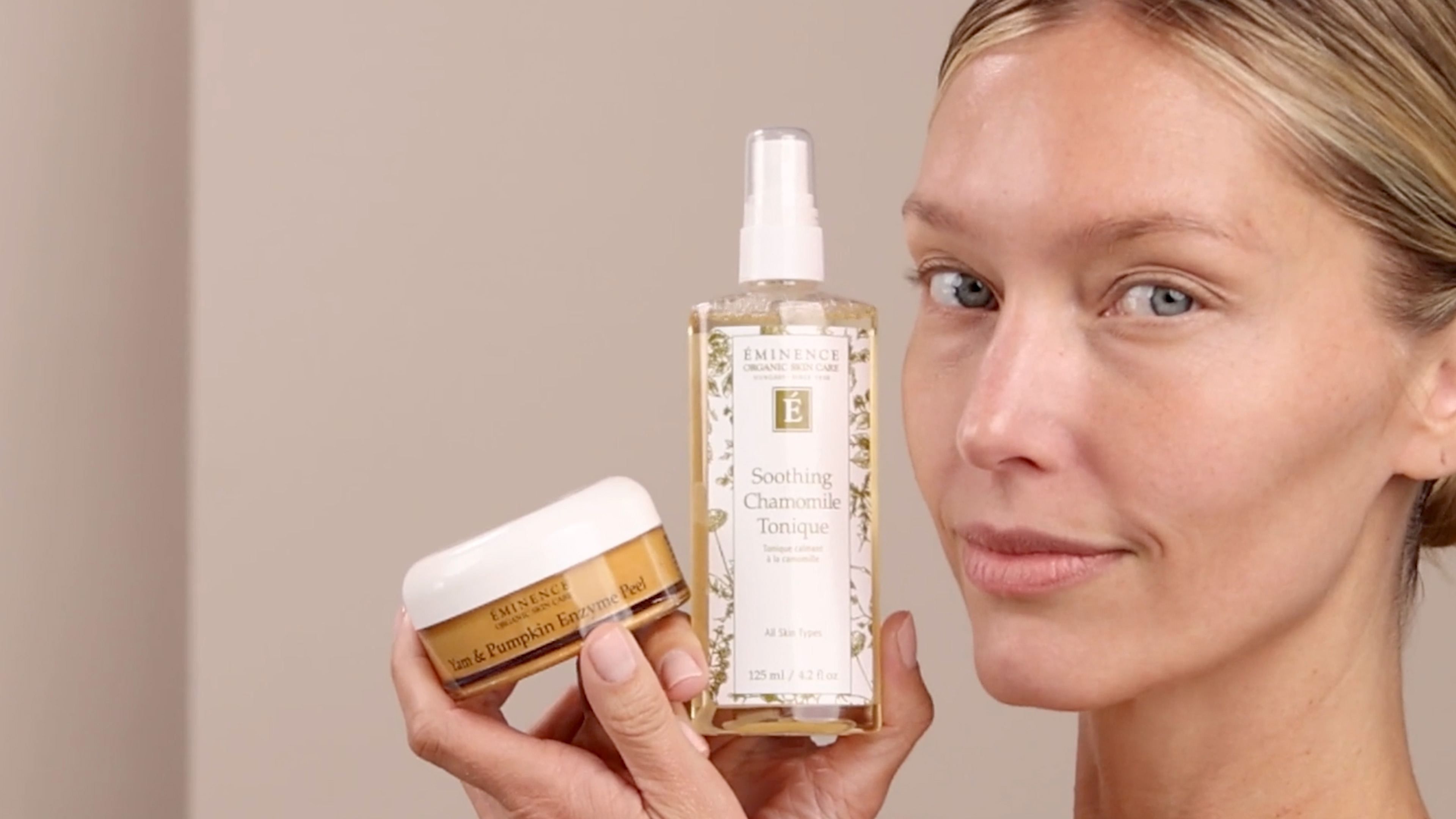 A woman holding the Eminence Organics Yam & Pumpkin Enzyme Peel 5% Swatch and the Eminence Organics Soothing Chamomile Tonique