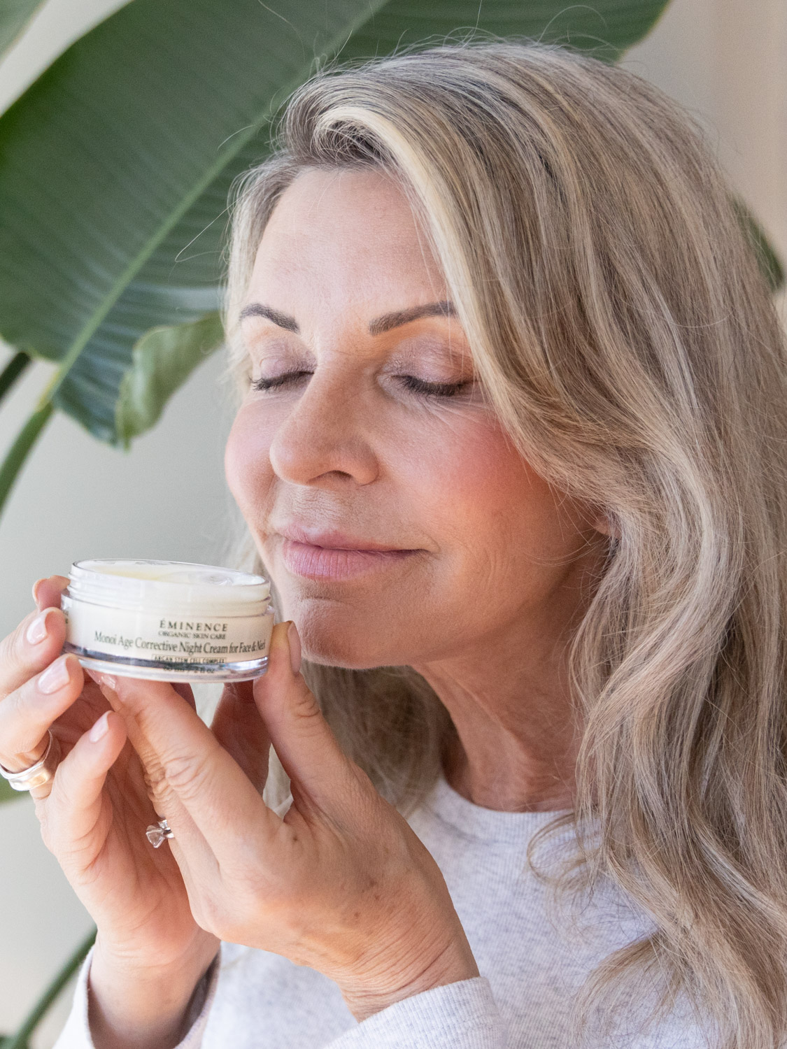 A woman smelling the Eminence Organics Monoi Age Corrective Night Cream for Face & Neck