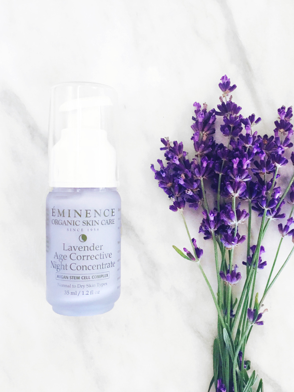 The Eminence Organics Lavender Age Corrective Night Concentrate glass bottle beside lavender plant