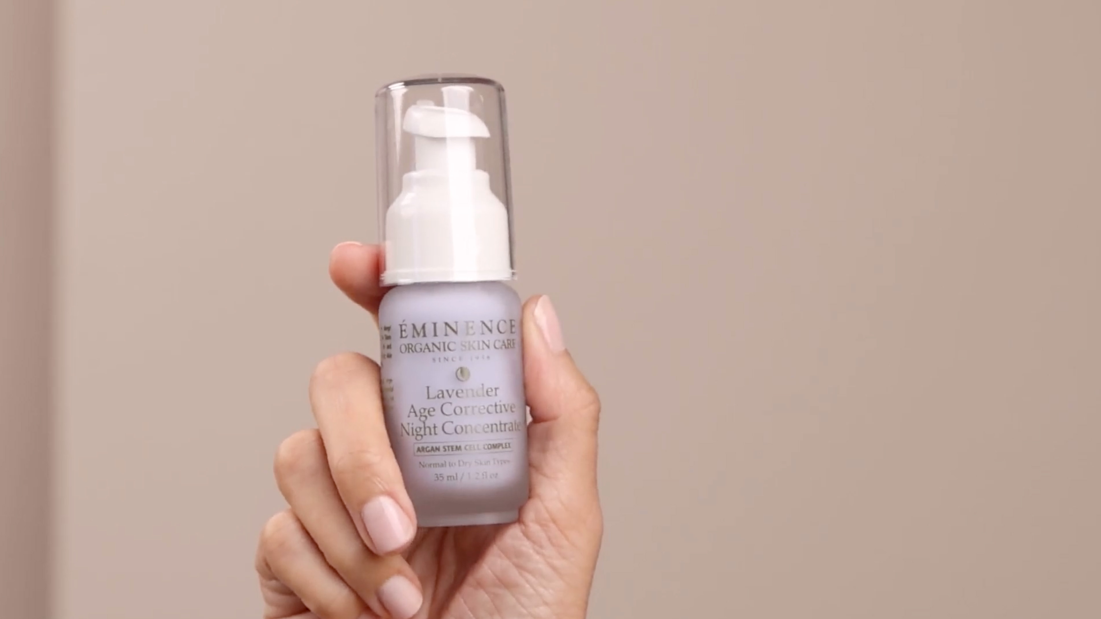 A hand holding the Eminence Organics Lavender Age Corrective Night Concentrate glass bottle