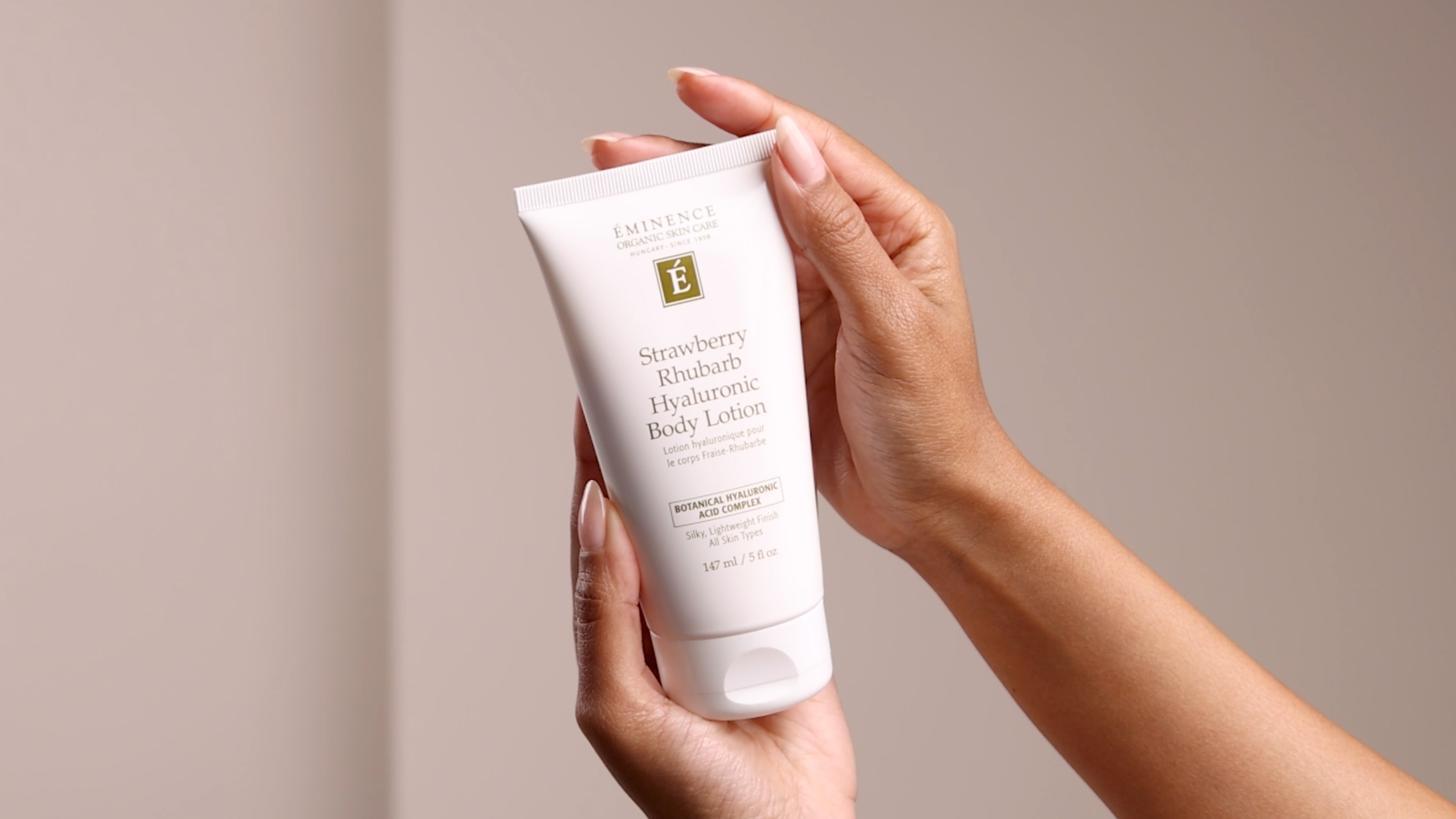 Hands holding the Eminence Organics Strawberry Rhubarb Hyaluronic Body Lotion