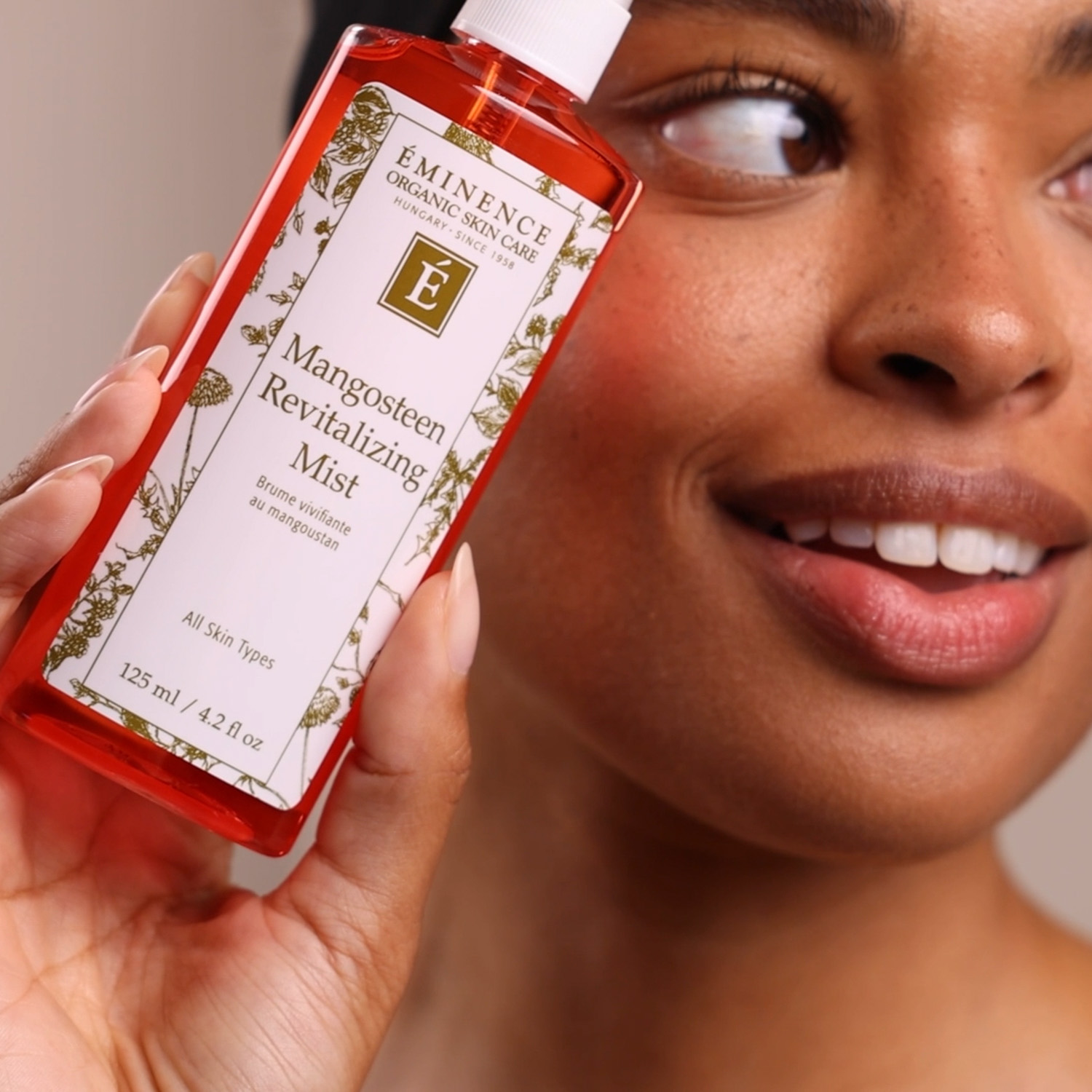 A woman holding the Eminence Organics Mangosteen Revitalizing Mist bottle next to their face