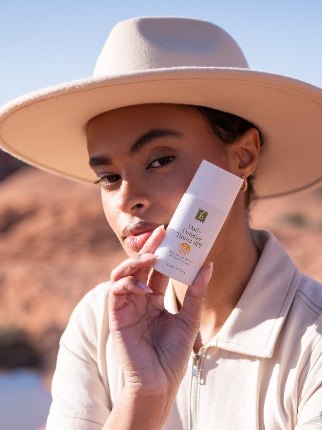 A woman holding the Eminence Organics Daily Defense Tinted SPF