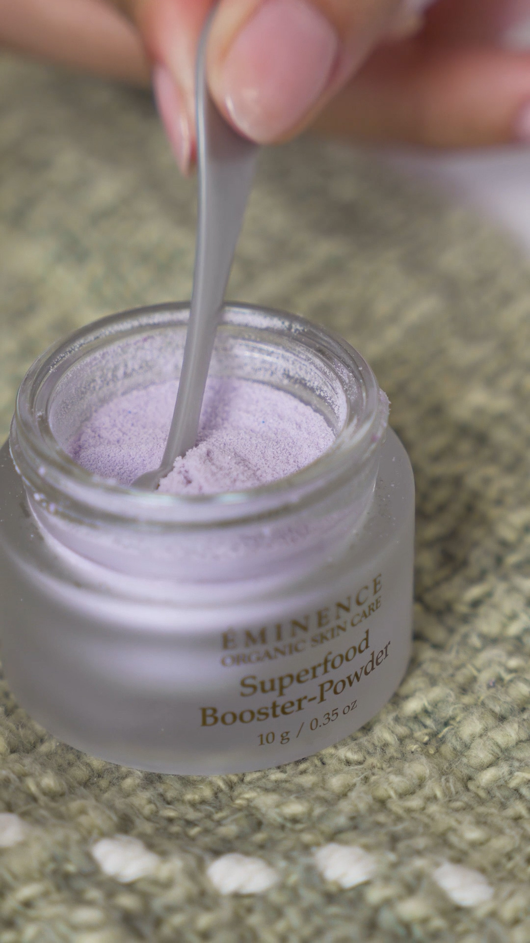 A hand dipping a spoon in the Eminence Organics Superfood Booster-Powder