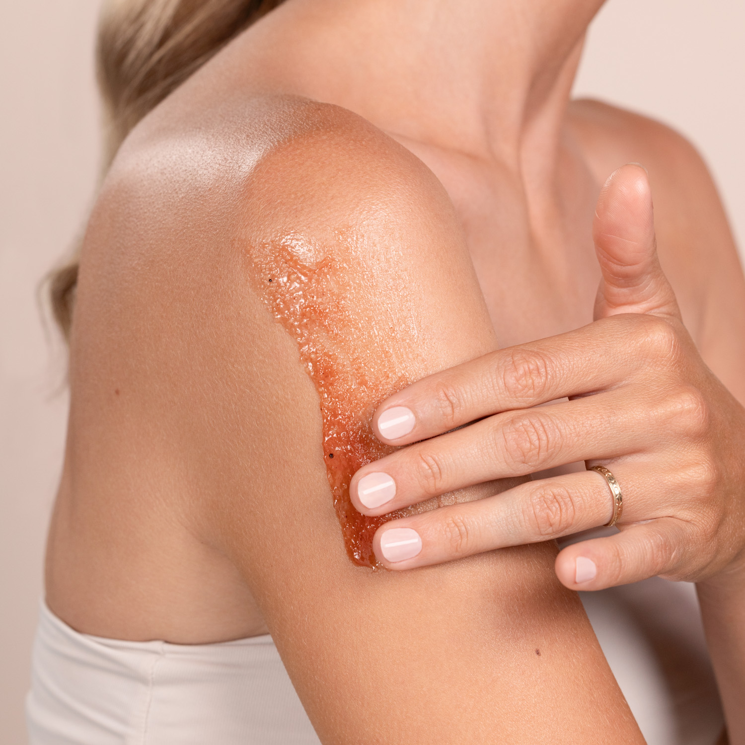 A woman applying the Eminence Organics Cranberry Pomegranate Sugar Scrub onto her shoulder