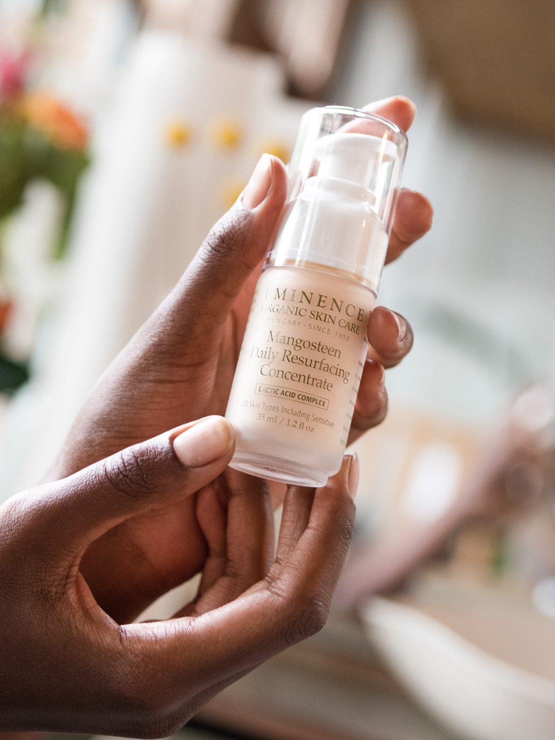 Two hands holding the Eminence Organics Mangosteen Daily Resurfacing Concentrate glass bottle