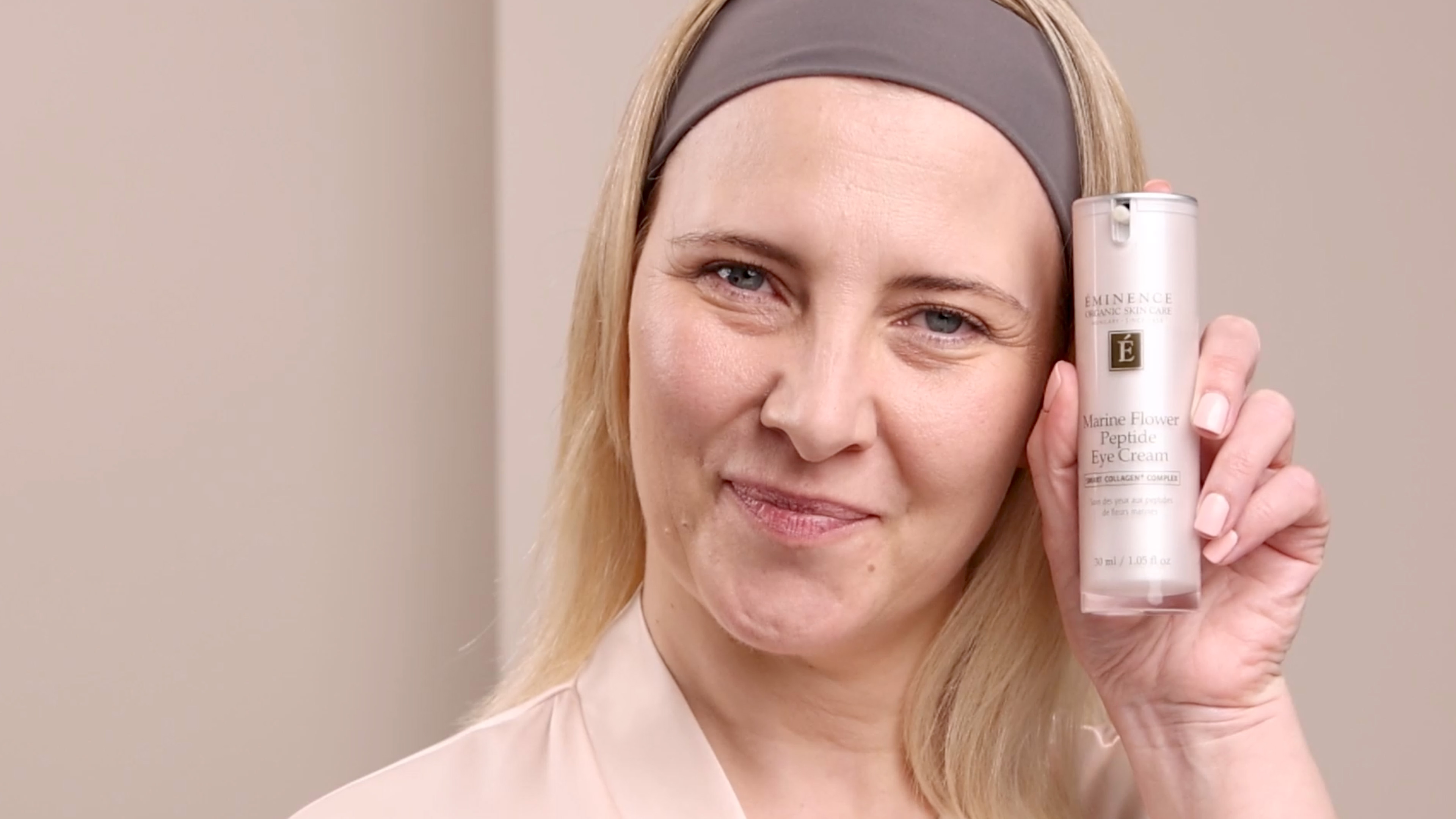 A woman holding the Eminence Organics Marine Flower Peptide Eye Cream Bottle next to their face