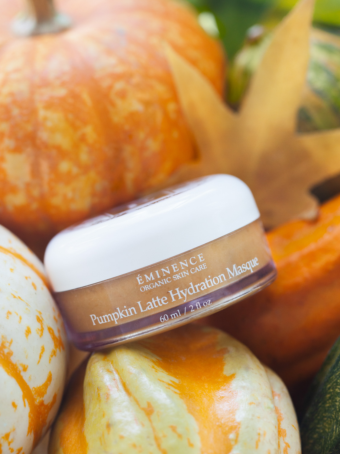 An Eminence Organics Pumpkin Latte Hydration Masque Jar surrounded by pumpkins
