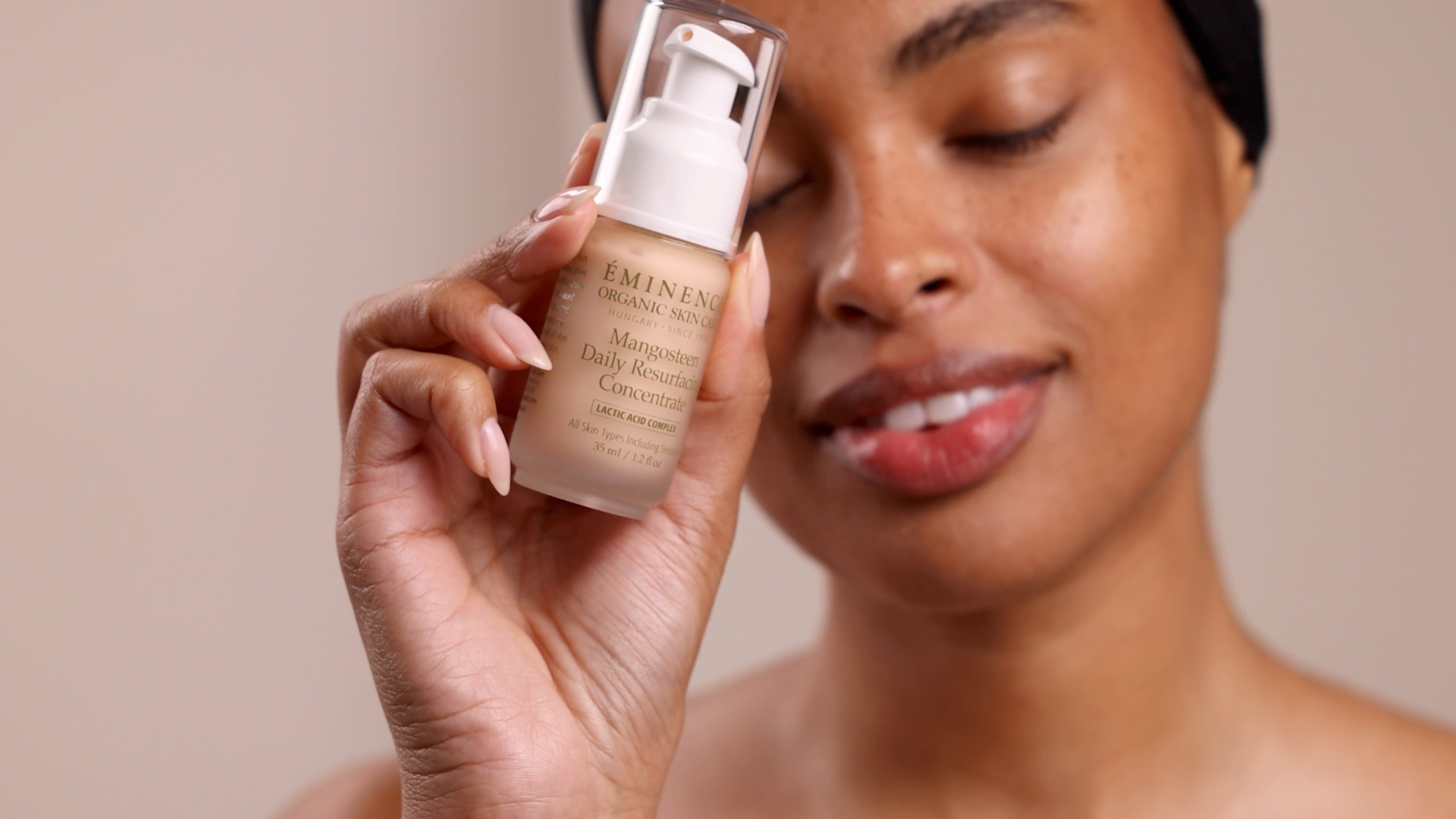 A woman holding the Eminence Organics Mangosteen Daily Resurfacing Concentrate glass bottle next to their face