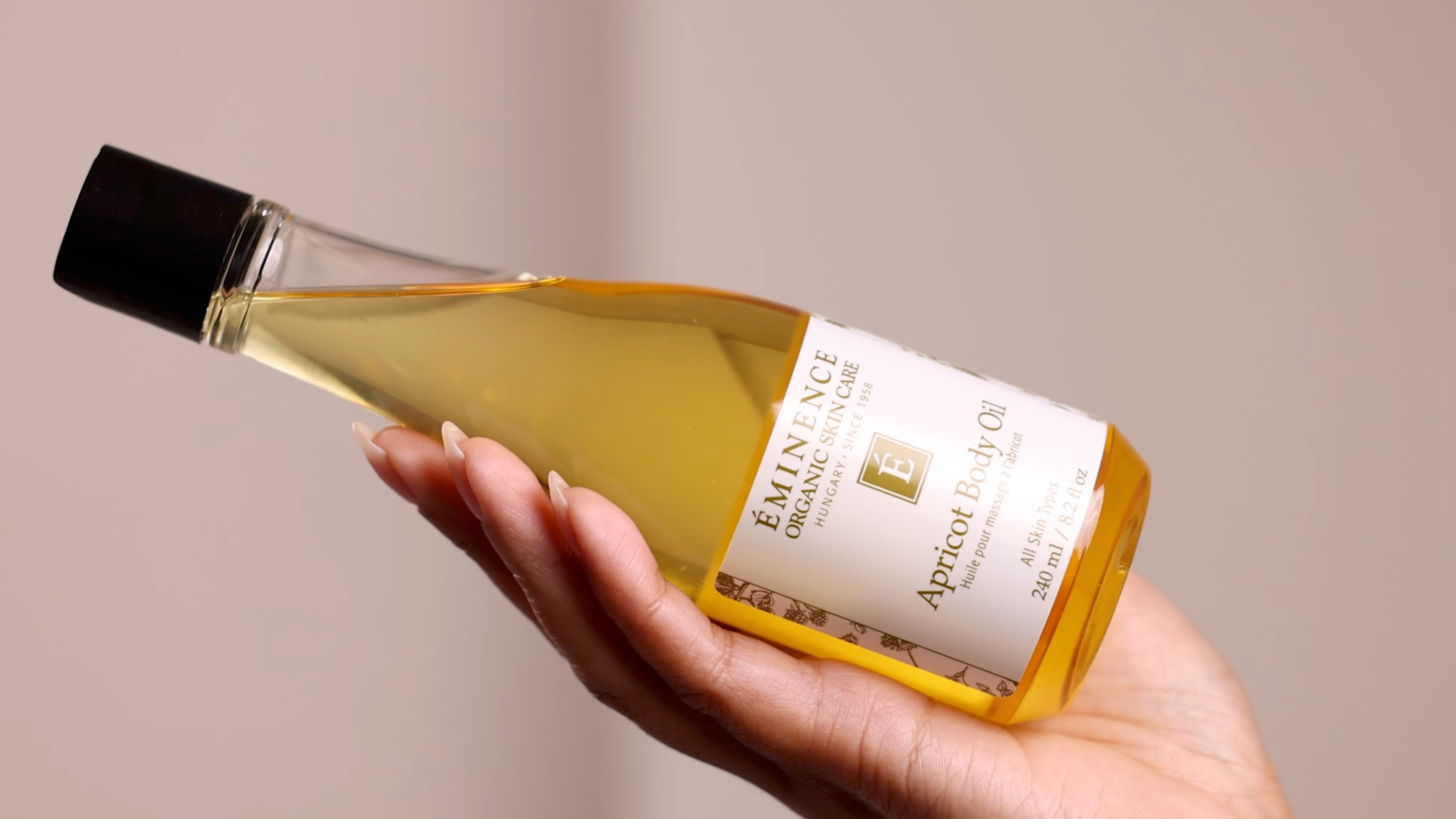 A woman's hand holding Eminence Organics Apricot Body Oil