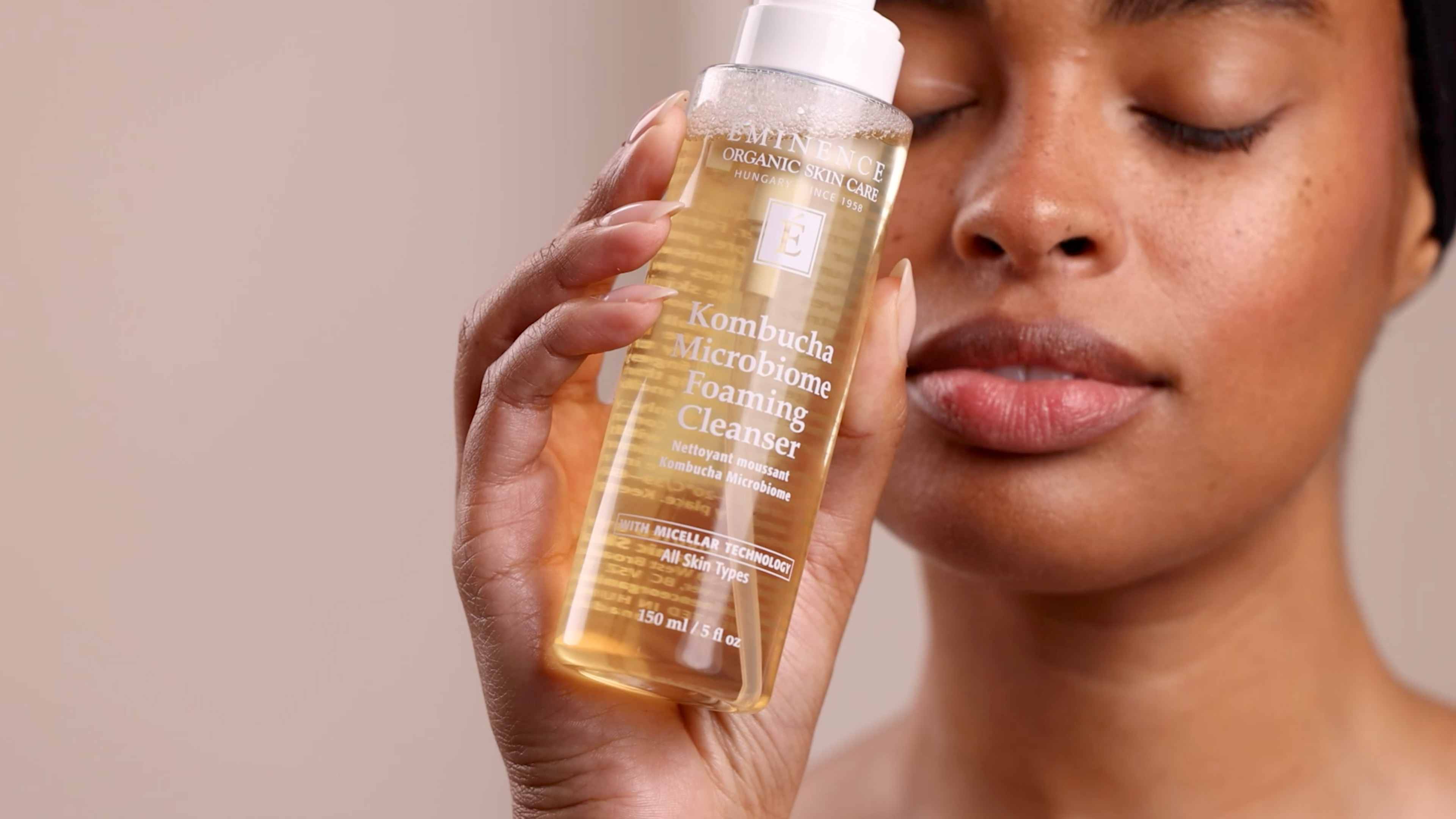 A woman holding the Eminence Organics Kombucha Microbiome Foaming Cleanser bottle