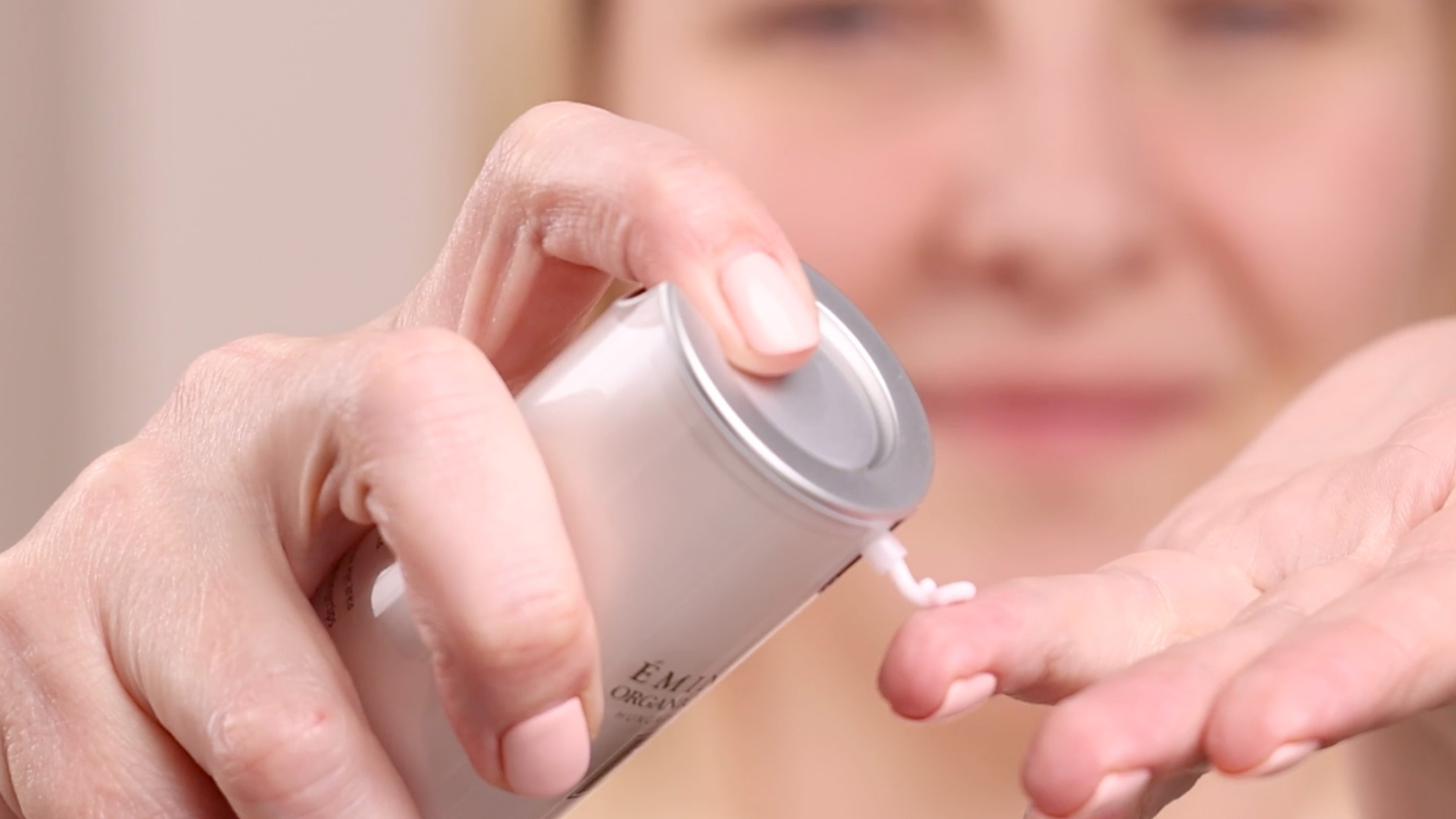 A woman dispensing a small amount of the Eminence Organics Wild Plum Eye Cream onto her hand from a pump component