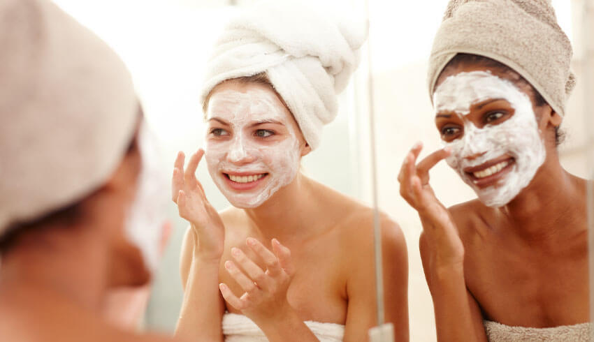 Two women applying cosmetic face masks in mirror