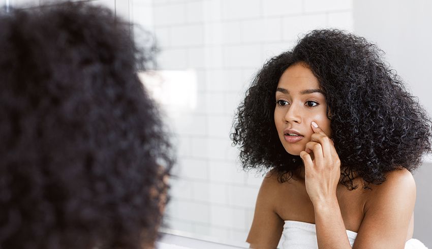 Woman touches her face while looking in the mirror at her reflection