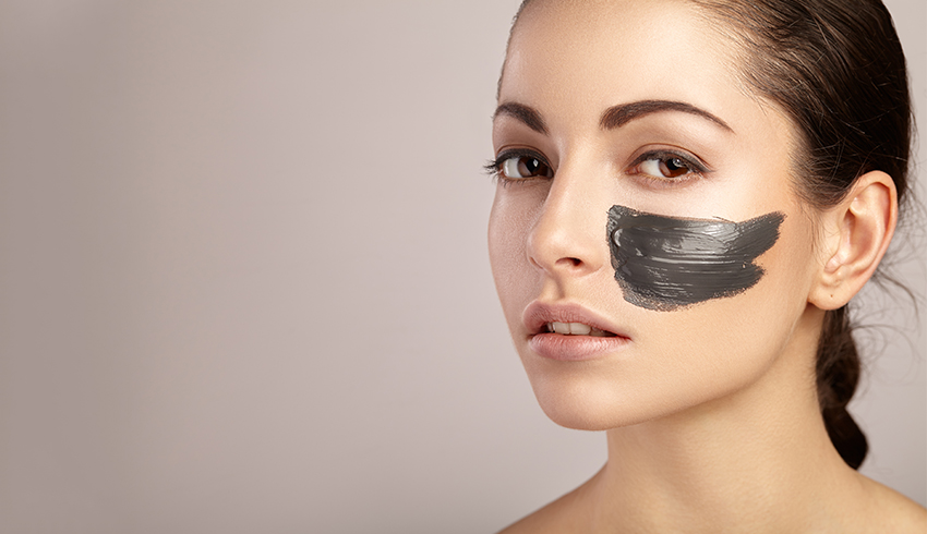 Woman with charcoal face mask on her left cheek
