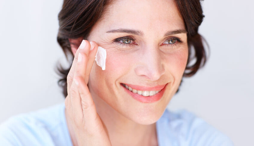 Woman smiling applying cream to face
