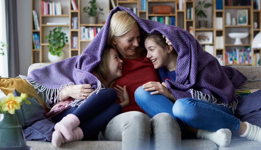 Mother and two kids playing under blanket at home 