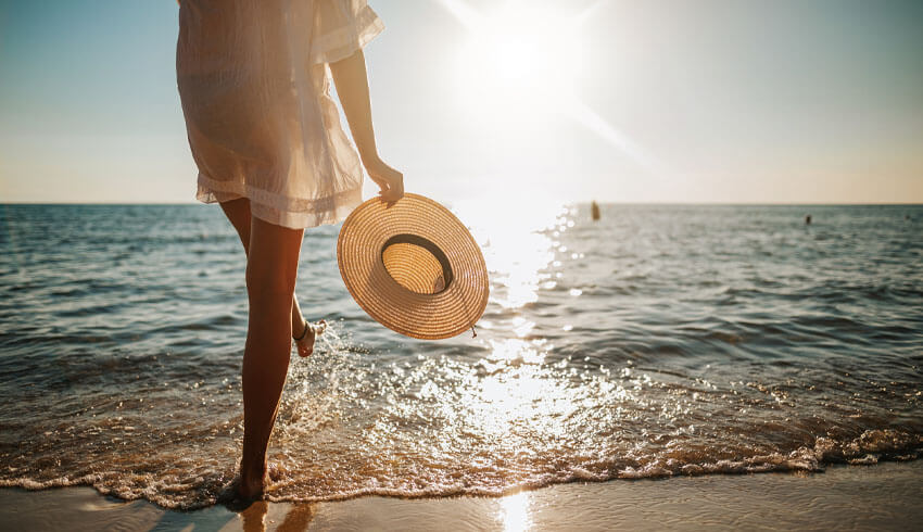 Woman standing in the ocean with a sun hat and sun shining