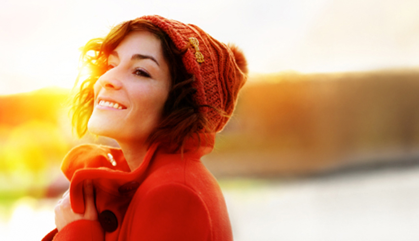 A smiling woman wearing a red knit hat and coat outside. 