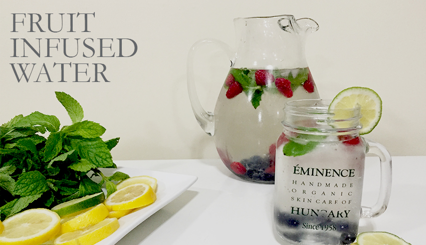 A picture and a Mason mug filled with fruit-infused water displayed next to a plate containing lemon and lime slices and mint leaves. 