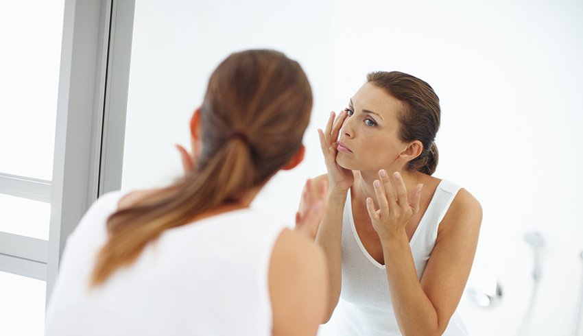 Woman looking in the mirror at the dark circles under her eyes