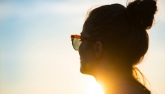 A woman wearing sunglasses gazes into the bright sun. 