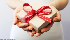A woman's outstretched hands holding a gift box tied with a red bow. 