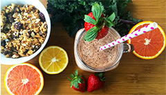 A breakfast smoothie garnished with a strawberry and a bowl of granola. 