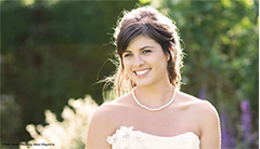 A smiling bride wearing a white strapless dress and a pearl necklace. 