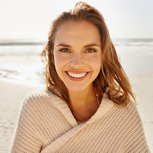 Smiling woman wrapped in beige sweater at the beach.