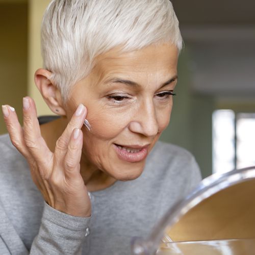 mature woman applying skin care product to treat acne