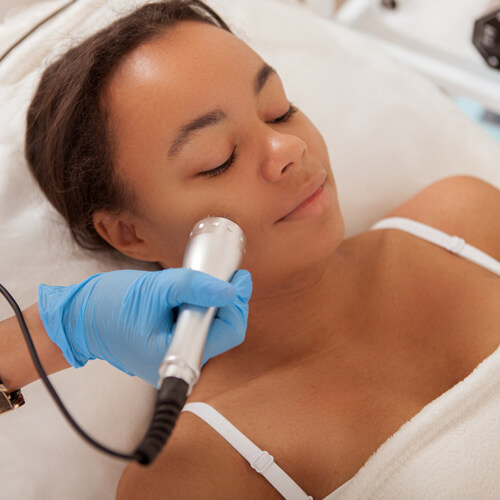 A woman lwith her eyes closed and lying on her back while receiving a microcurrent facial. 