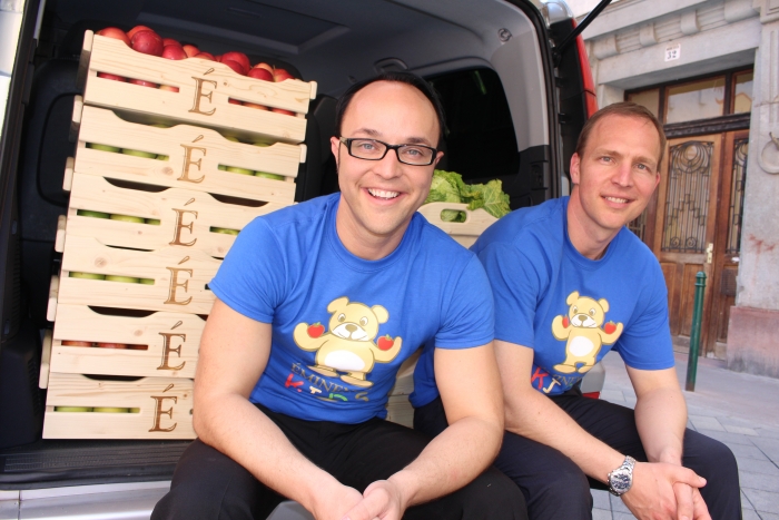 Eminence Organic Skin Care President, Boldijarre Koronczay and General Manager Attila Koronczay seated on the back bumper of a delivery van with its rear doors open. Inside, the van is filled with donations of boxes of fresh fruit and vegetables. from the Eminence Kids Foundation. 